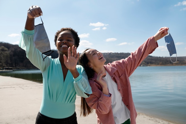 Two female friends celebrating the lifting of face mask restrictions outdoors together