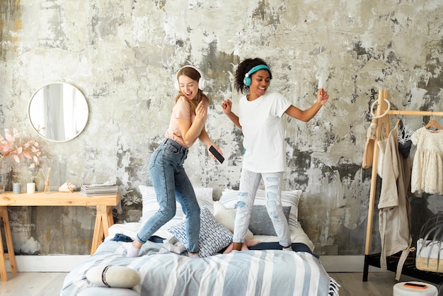 Free Photo two female friends dancing together on bed while listening to music