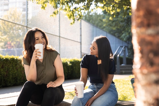 Two female friends having a cup of coffee together at the park