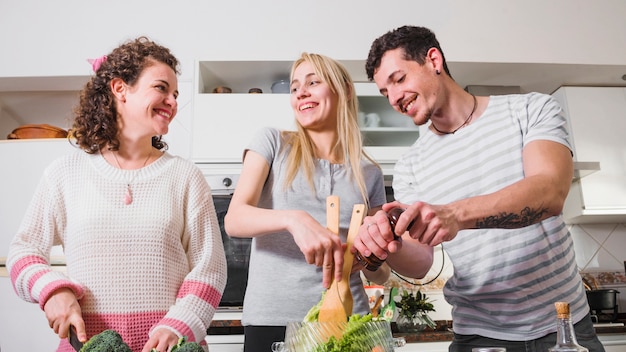 Two female friends and her man preparing salad in the kitchen