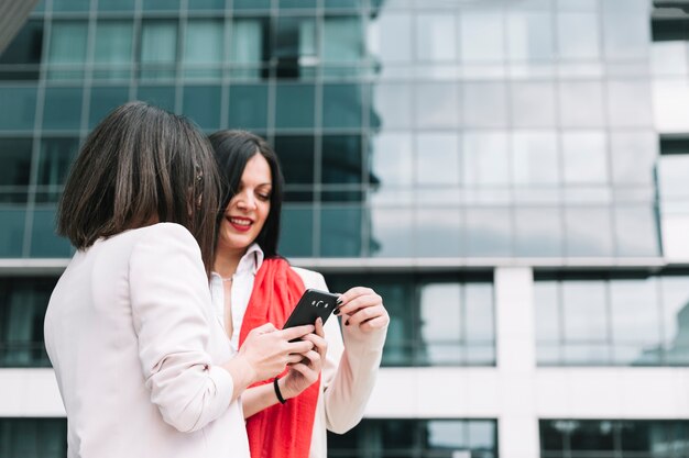 Two female friends looking at mobile phone with building in background