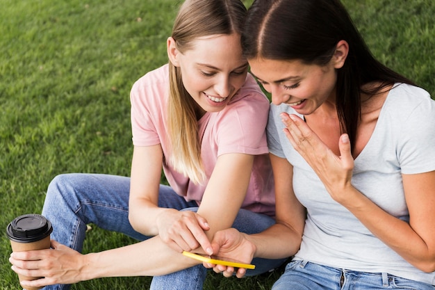 Free photo two female friends looking through smartphone outdoors