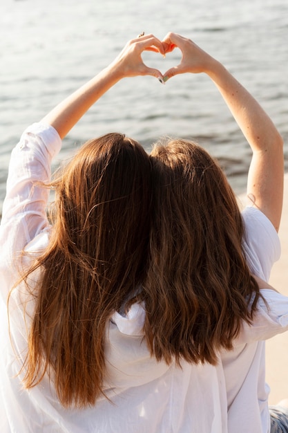 Free Photo two female friends making the love sign by the lake