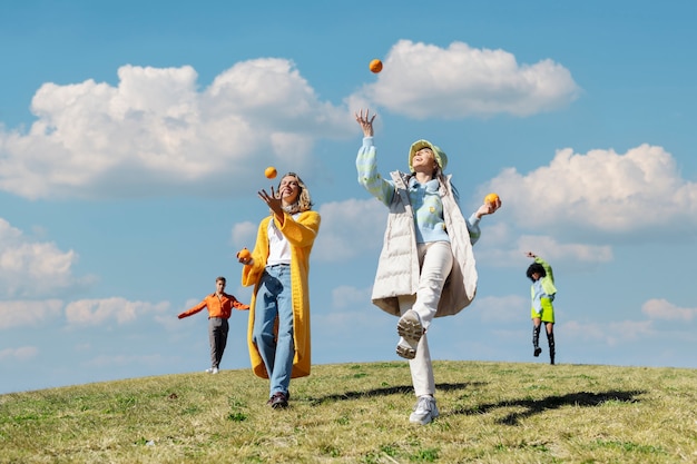 Two female friends playing with oranges and other two dancing in an outdoor field