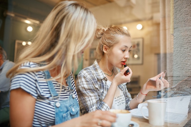 Two female friends sitting inside cafe and having coffee