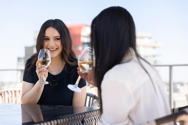 Two female friends spending time together and drinking wine on a rooftop terrace