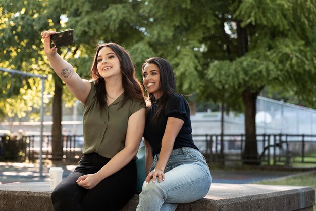 Two female friends taking selfie in the park while having some coffee