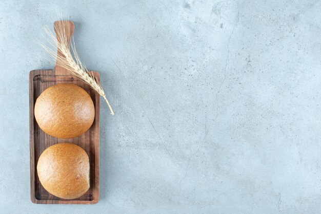 Free photo two fresh buns on wooden board with wheat.