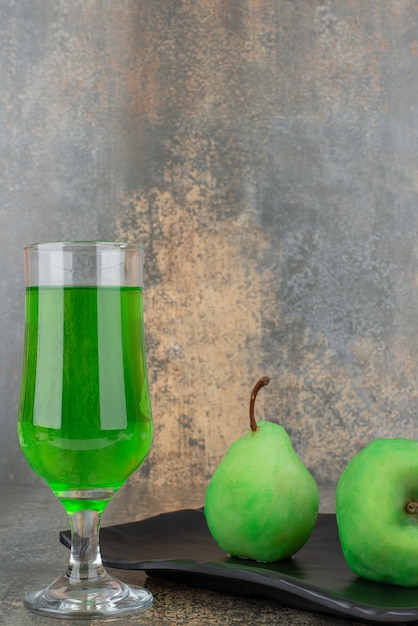 Free photo two fresh green apples with glass of green water on dark plate