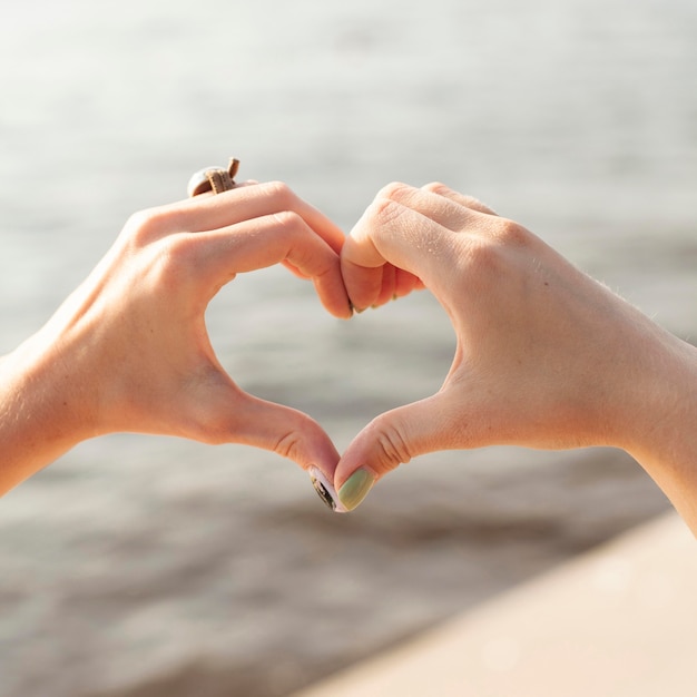 Free photo two friends making heart sign at the lake with hands