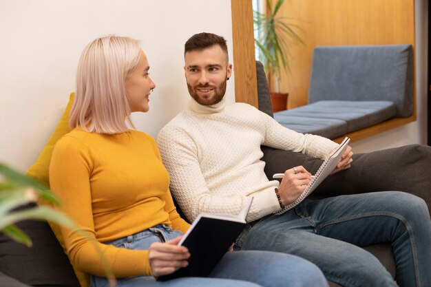 Two friends reading from a book and a notebook in a library