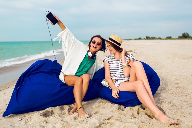 Two friends siting on beach pillows, having fun