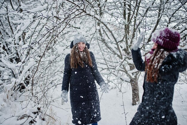 Two funny girls friends having fun at winter snowy day near snow covered trees