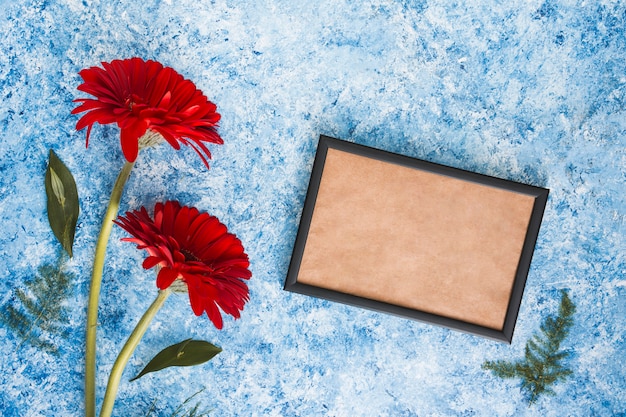 Free photo two gerbera flowers with blank frame on table