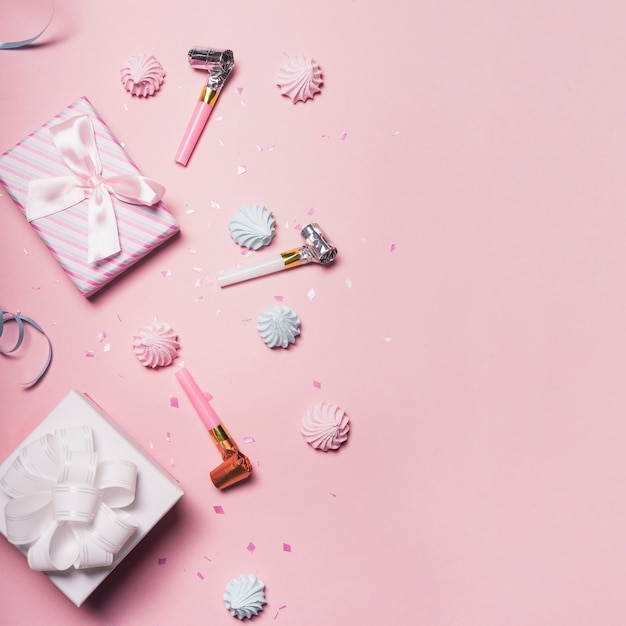 Two gift boxes with whipped cream; confetti and party blower on pink background