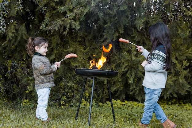 Two girls cooking sausages in barbecue at outdoors