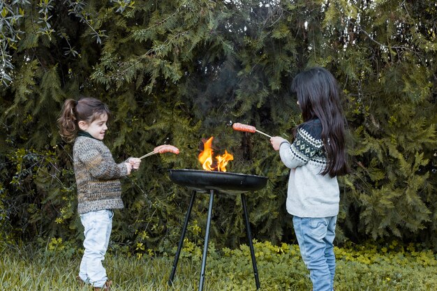 Two girls grilling sausages in barbecue