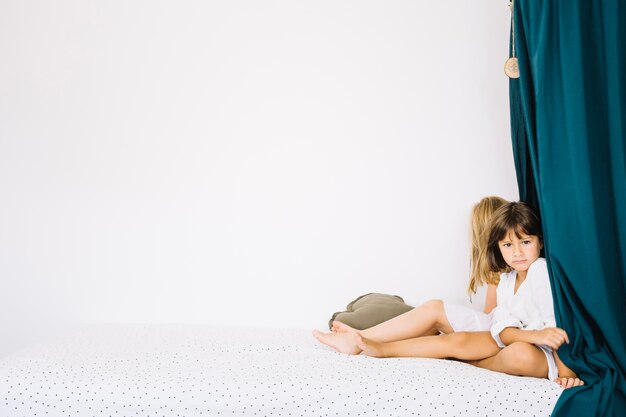 Two girls near curtains on bed