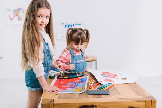 Free photo two girls painting with aquarelle on paper