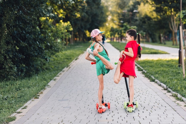 Two girls standing over the kick scooter stretching their legs