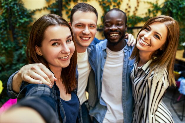 Two girls and two boys are taking selfie picture outdoors, hugging each other and with sincere smiles