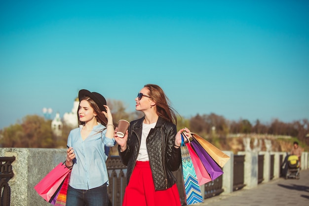 Two girls walking with shopping bags on city streets at sunny day