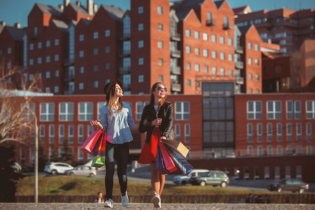 Free photo two girls walking with shopping bags on city streets at sunny day