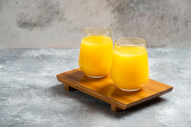 Free photo two glass cups of fresh orange juice on wooden board.