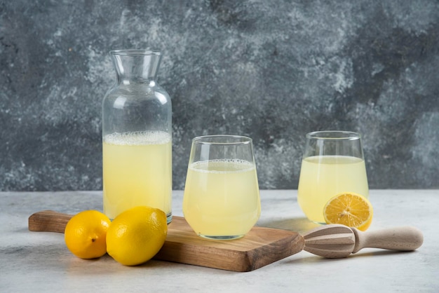 Two glass cups of lemon juice and jar on a wooden board.