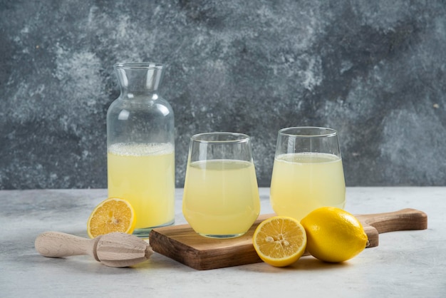 Two glass cups of lemon juice and jar on a wooden board.