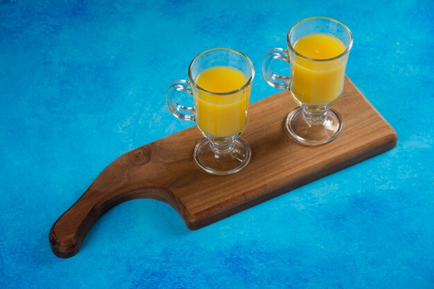 Free photo two glass cups of orange juice on wooden board.