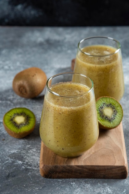 Free photo two glass cups of tasty kiwi juice on wooden board.