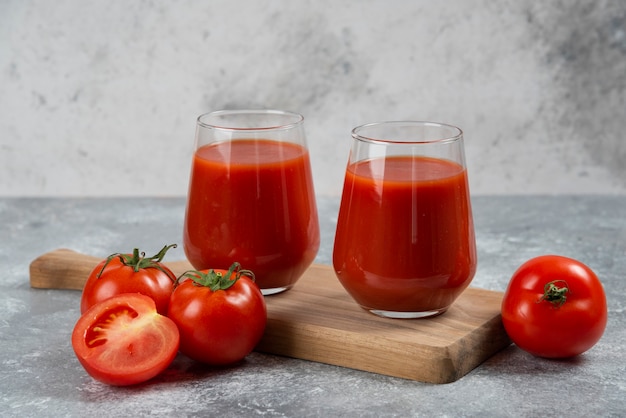 Two glass cups of tomato juice on a wooden board.