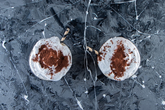 Free photo two glasses of coffee with whipped cream on marble surface.