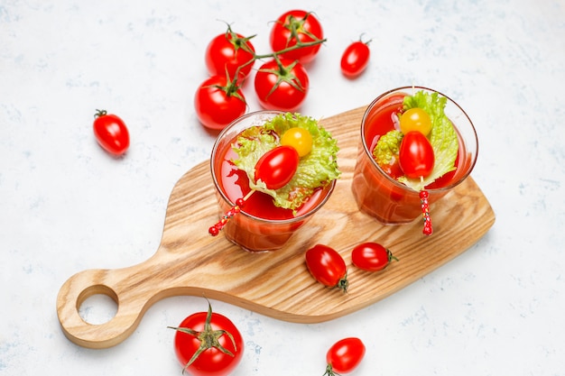 Two glasses of fresh tomato juice and tomatoes on gray concrete surface