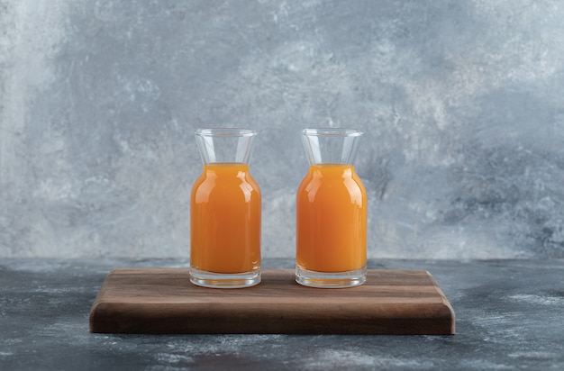 Two glasses of orange juice on wooden board. 