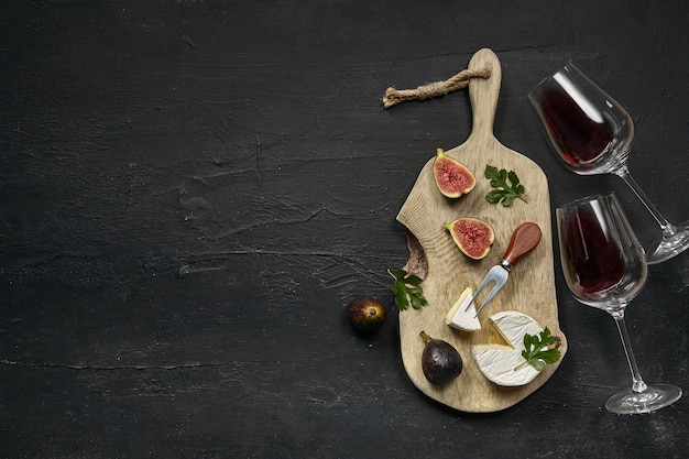 Free Photo two glasses of red wine and a tasty cheese plate with fruit on a wooden kitchen plate on the black stone