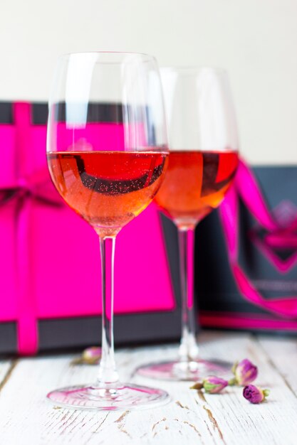 Two glasses of rose wine on white wooden table with pink gift boxes 