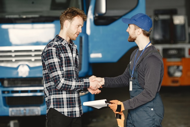 Free photo two guys talking about work. work in garage near truck. transfer of documents with goods