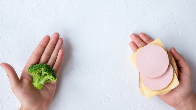 Two hands holding broccoli and a sandwich. Healthy food idea. Light background