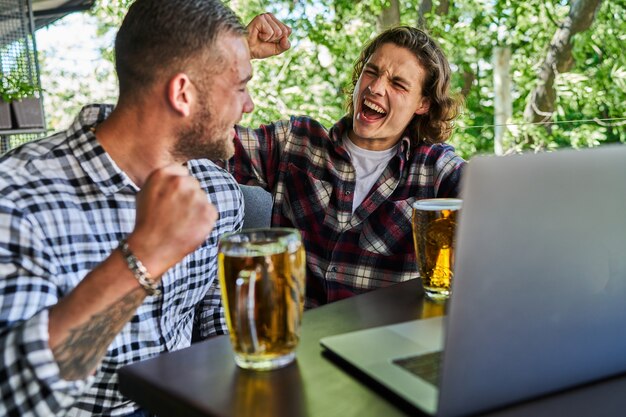 Two handsome men watching football in a pub and drinking beer.