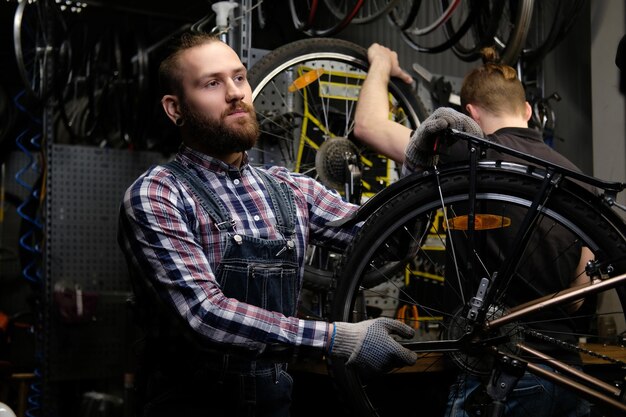 Two handsome stylish males working with a bicycle in a repair shop. Workers repair and mounts bike in a workshop.