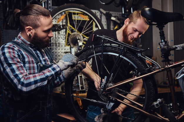 Two handsome stylish males working with a bicycle in a repair shop. Workers repair and mounts bike in a workshop.