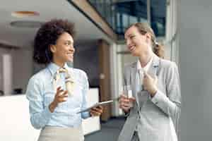 Free photo two happy businesswomen communicating while standing in a hallway