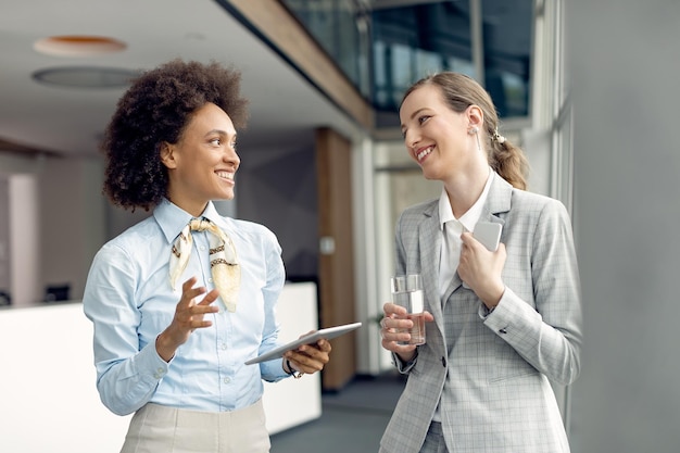 Two happy businesswomen communicating while standing in a hallway