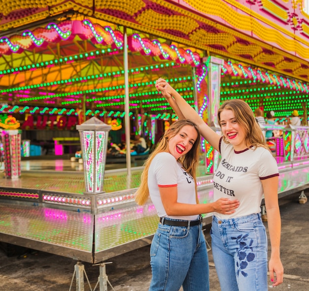 Free Photo two happy female friends raising their arms at amusement park