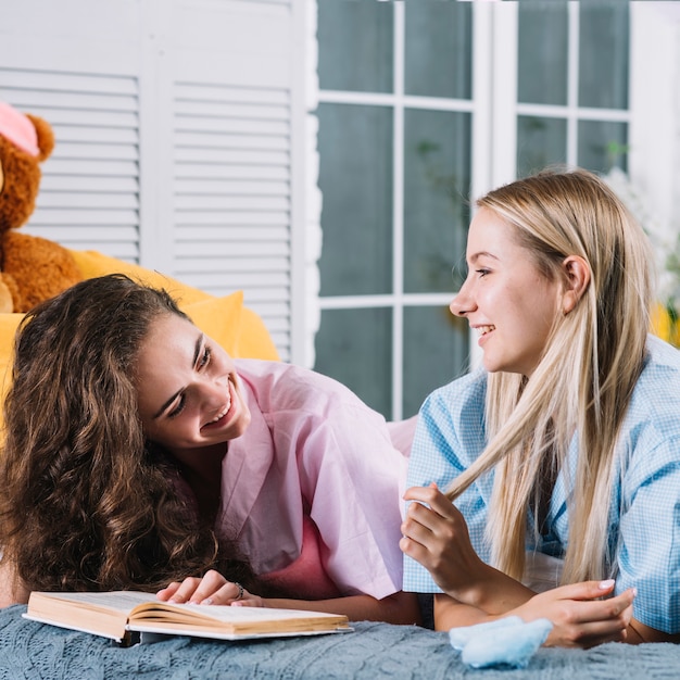 Free photo two happy female friends with book looking at each other