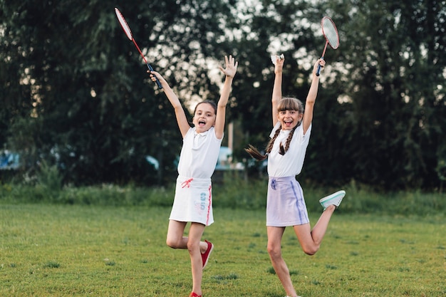 Two happy girls holding badminton jumping in the park with joy