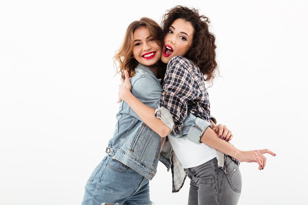 Two happy girls hugging to each other  over white wall