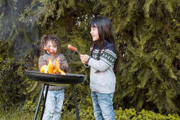 Two happy girls roasting sausages on portable barbecue